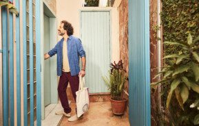 A foto mostra um homem entrando em um apartamento. Ele sorri e está feliz.