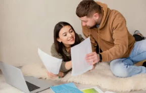Imagem de um homem e uma mulher sentados no chão olhando alguns documentos em frente a um notebook para ilustrar matéria sobre o que é ITCMD.