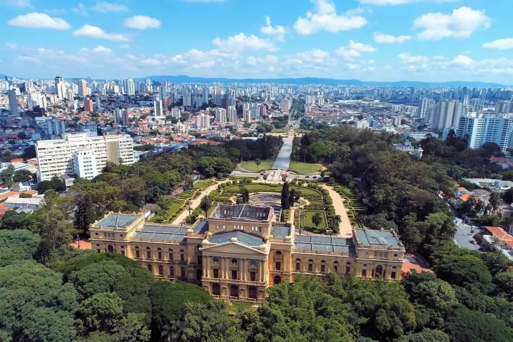 Imagem da vista aérea do Parque da Independência, em São Paulo, mostra vegetação que cerca o Museu do Ipiranga, além de prédios ao fundo, para ilustrar matéria sobre os melhores parques de São Paulo