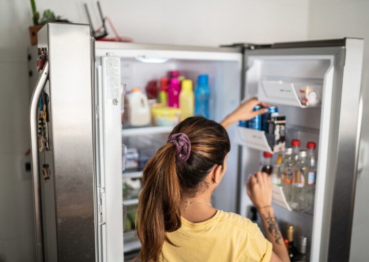 Imagem que ilustra matéria sobre como organizar geladeira mostra uma mulher colocando uma latinha de refrigerante na porta de sua geladeira.