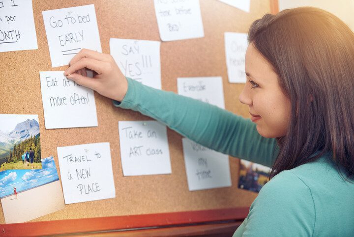 Imagem de uma mulher pendurando post it com metas e objetivos em um quadro dos sonhos.