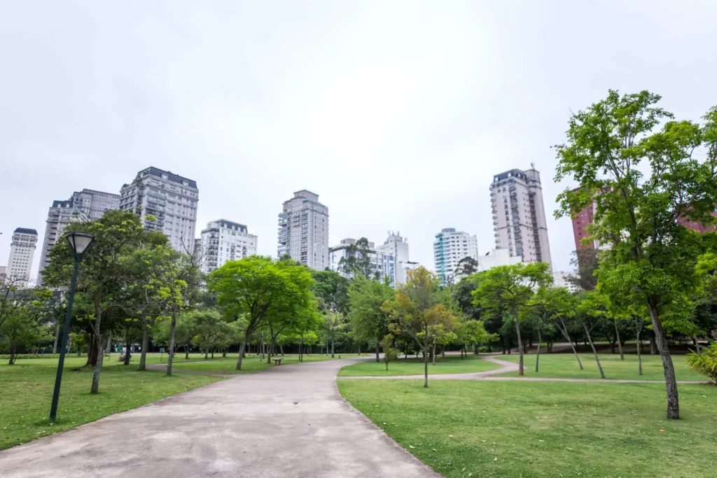 Imagem da pista de caminhada, gramado e árvores do Parque do Povo com prédios ao fundo para ilustrar matéria sobre parques de SP
