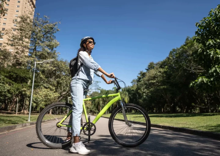 Imagem de uma mulher parada em cima de uma bicicleta com as mãos no guidão olhando para o horizonte em uma ciclovia rodeada por árvores para ilustrar matéria sobre os parques em SP
