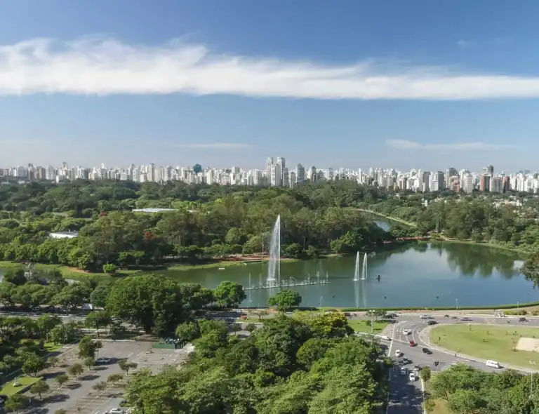 Imagem da vista aérea do Parque Ibirapuera mostra vegetação, lago e fonte do espaço, além de prédios ao fundo, para ilustrar matéria sobre os parques gratuitos em SP