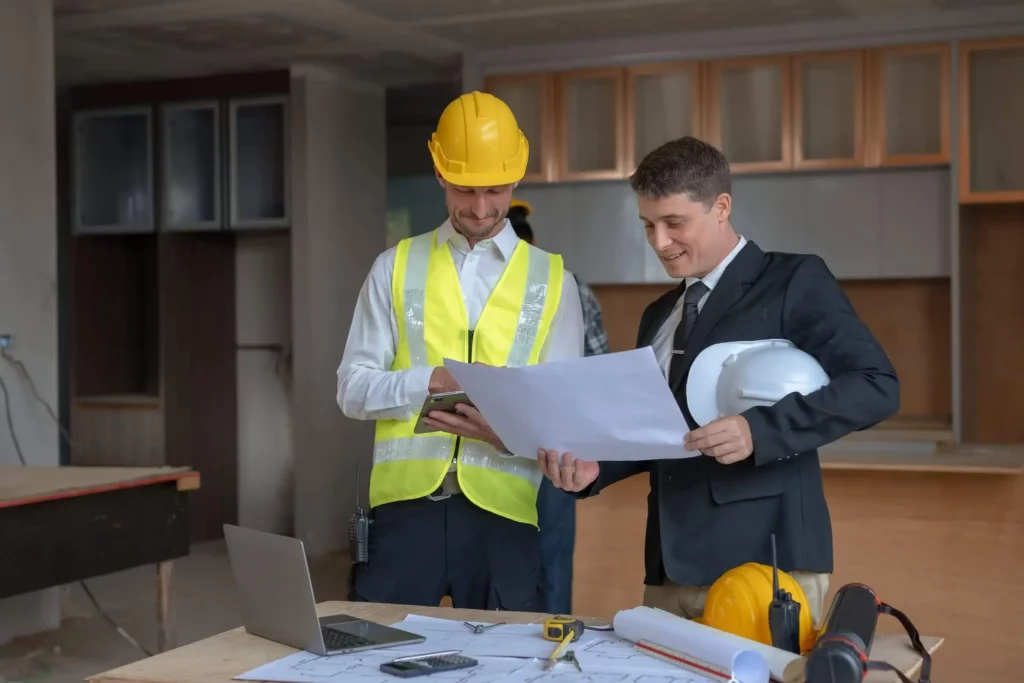 Imagem de um engenheiro e um arquiteto trabalhando juntos na reforma de um edifício em um canteiro de obras para ilustrar matéria sobre quanto custa reformar um apartamento de 100m2
