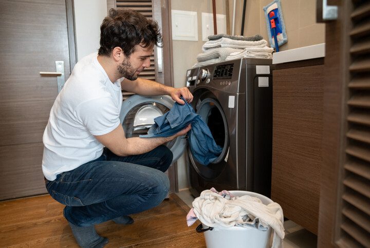 Homem colocando roupas para lavar na máquina.