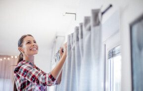 Mulher feliz instalando uma cortina em casa.