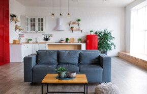 Imagem de uma sala moderna integrada com uma cozinha em tons de cinza, branco, madeira e vermelho.