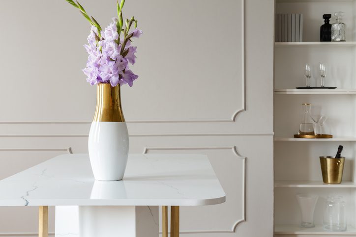 Flores roxas em um vaso de ouro, em uma mesa de mármore branco.