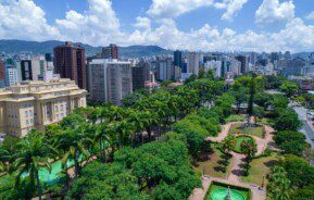 Foto que ilustra matéria sobre como é morar em Belo Horizonte uma vista do alto da Praça da Liberdade, com muitas do centro para o lado direito da imagem. Do centro para a esquerda, aparece em destaque o CCBB e muitos prédios, além de montanhas ao fundo.