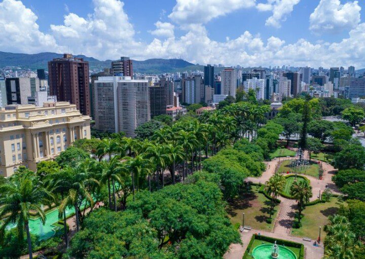 Foto que ilustra matéria sobre como é morar em Belo Horizonte uma vista do alto da Praça da Liberdade, com muitas do centro para o lado direito da imagem. Do centro para a esquerda, aparece em destaque o CCBB e muitos prédios, além de montanhas ao fundo.