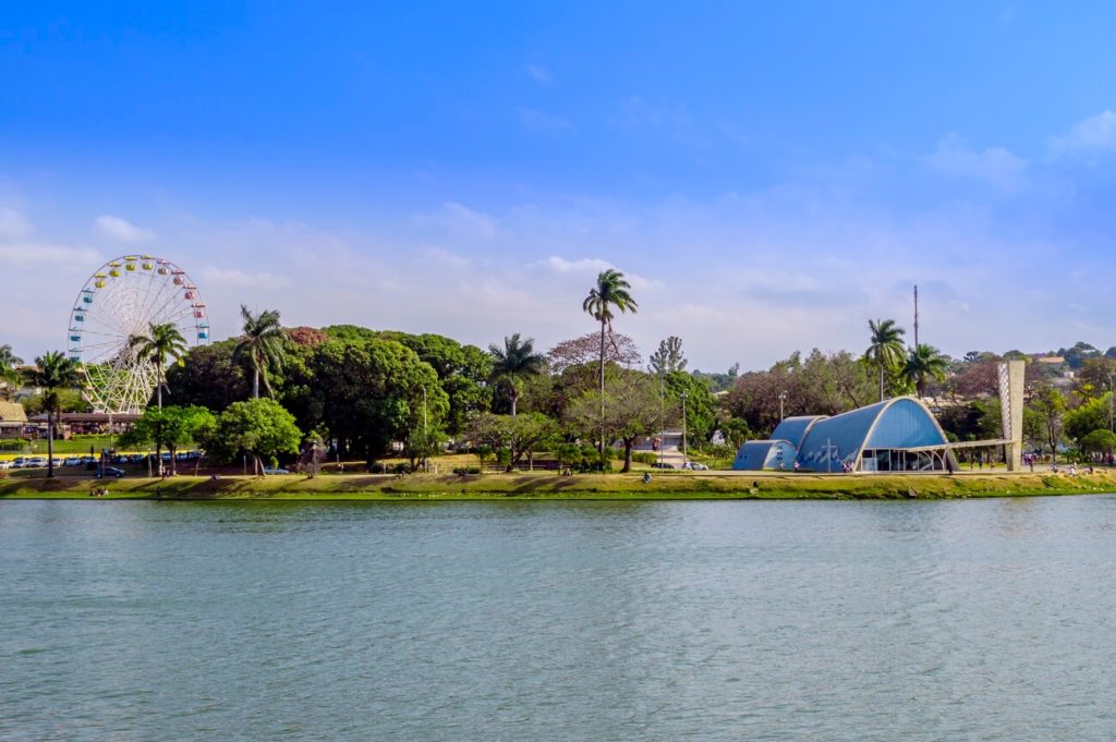 Foto que ilustra matéria sobre morar em Belo Horizonte mostra uma visão da orla da Lagoa da Pampulha, com destaque para a Igreja da Pampulha e a roda gigante do Parque Guanabara.