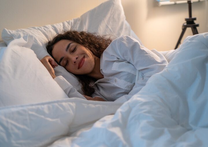 Mulher dormindo em uma cama com roupa de cama toda branca.