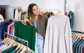 Foto que ilustra matéria sobre onde comprar roupas baratas em Belo Horizonte mostra uma mulher em meio a araras repletas de roupas penduradas em uma loja