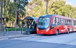 Foto que ilustra matéria sobre transporte público em Curitiba mostra uma estação do BRT com um ônibus biarticulado ao lado