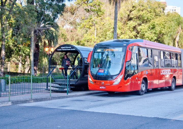 Foto que ilustra matéria sobre transporte público em Curitiba mostra uma estação do BRT com um ônibus biarticulado ao lado