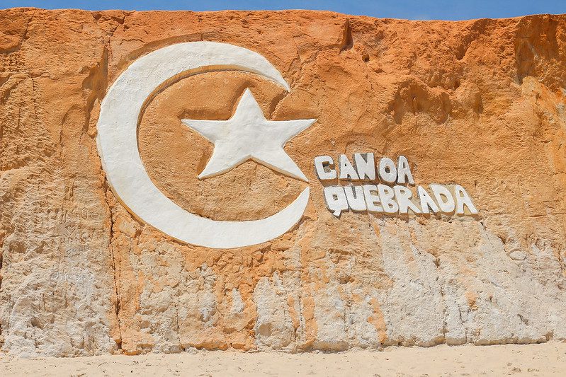 Foto de uma falésia onde tem escrito grande e em branco: Canoa Quebrada.