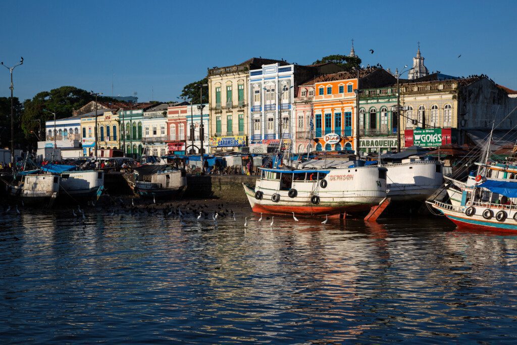 Imagem de vários barcos na doca do Mercado Ver o Peso, em Belém do Pará. Ao fundo, prédios construídos no estilo colonial e um céu azul