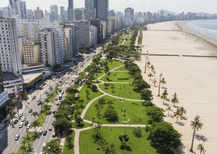 Foto que ilustra matéria sobre orla de Santos mostra a orla da cidade vista de cima, com extensa faixa de areia e uma parte do maior jardim de orla do mundo