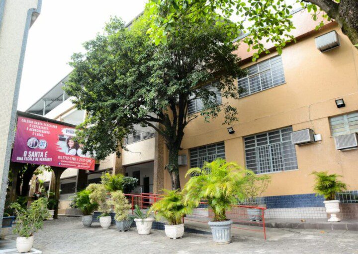 Foto que ilustra matéria sobre escolas em São Gonçalo mostra uma área interna do Colégio Santa Terezinha, com uma grande árvore diante de um prédio baixo