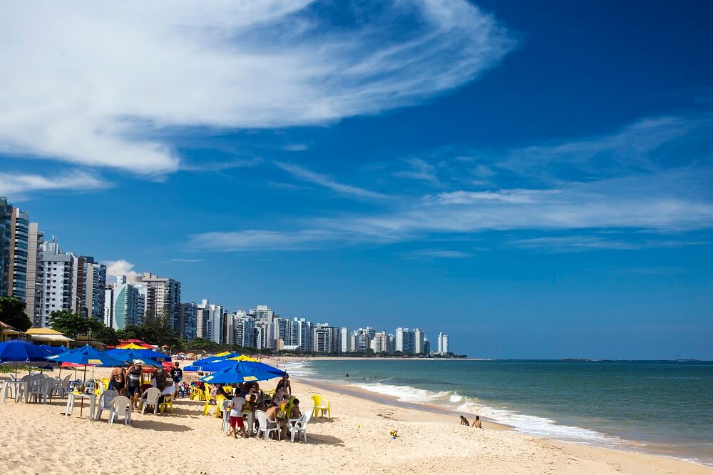 Foto que ilustra matéria sobre bairros de Vila Velha mostra uma visão panorâmica da Praia de Itaparica, com prédios no canto esquerdo, a faixa de areia e o mar no canto direito da imagem. (Foto: Vitor Jubini | MTur)