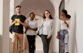 Imagem de quatro universitários sorridentes andando em um corredor de uma faculdade para ilustrar matéria sobre as faculdades do Rio de Janeiro
