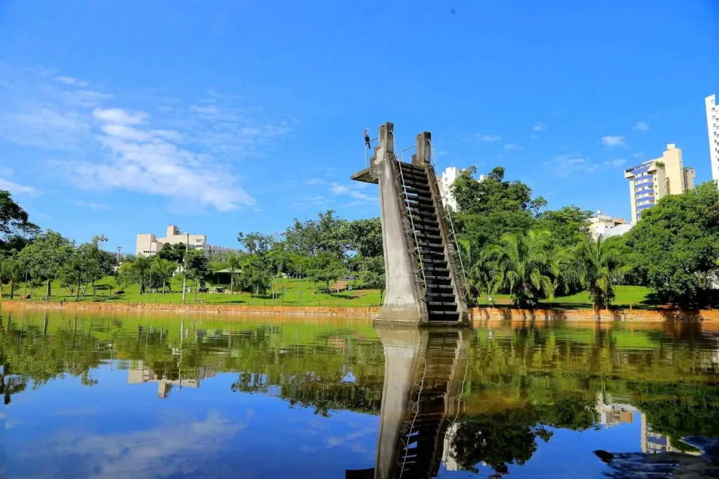 Imagem de lago, estrutura de concreto no meio do lago e vegetação ao redor da água no Parque Lago das Rosas, em Goiânia