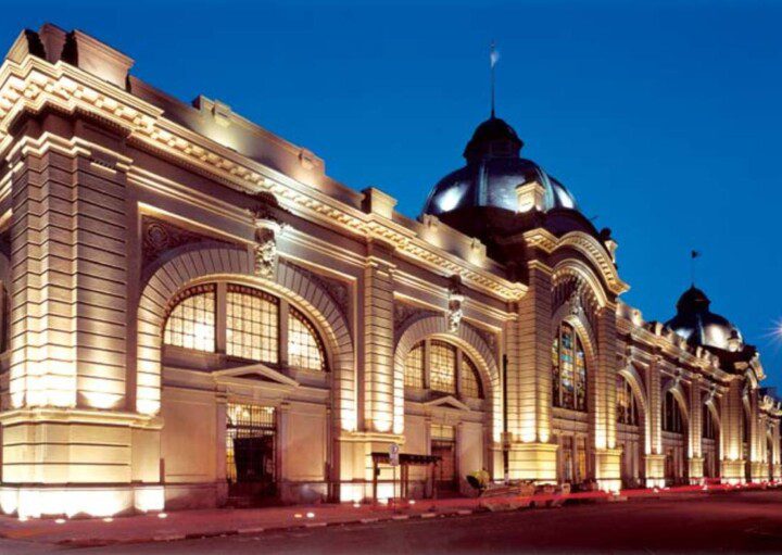 Imagem da fachada do Mercado Municipal de São Paulo a noite toda iluminada.