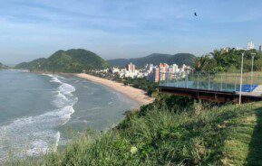 Imagem de um dos mirantes do Guarujá com estrutura em vidro e vista para a praia.