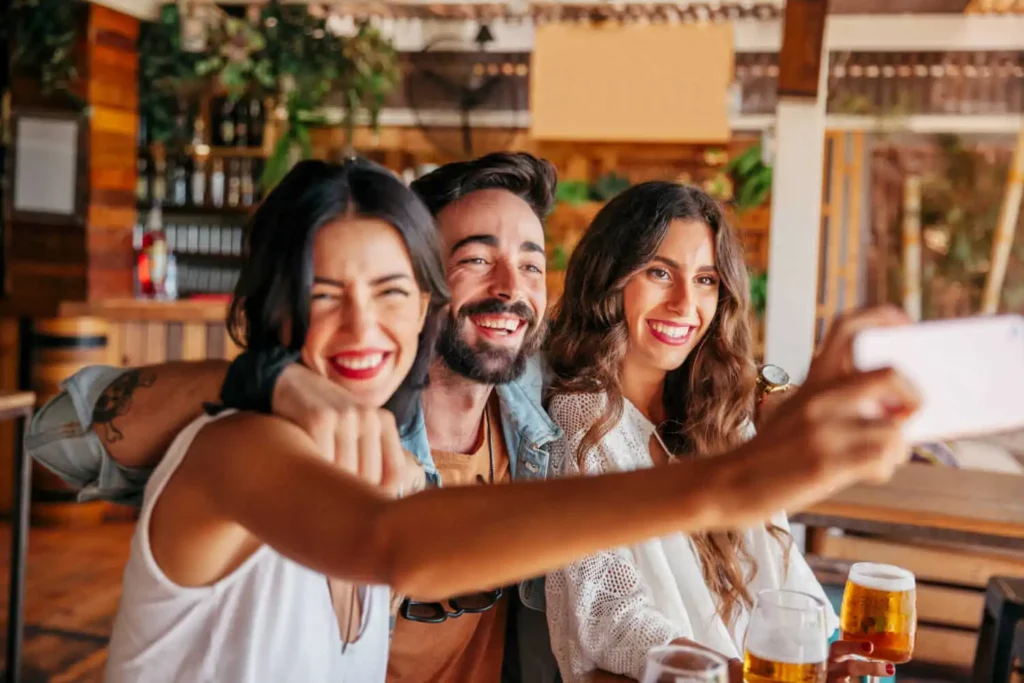Imagem de três amigos, duas mulheres e um homem, se abraçando enquanto tiram uma selfie na mesa de um bar para ilustrar matéria sobre o que fazer em Goiânia