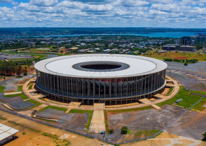 Foto que ilustra matéria sobre o Estádio Mané Garrincha mostra toda a arena vista de cima em um dia de céu azul