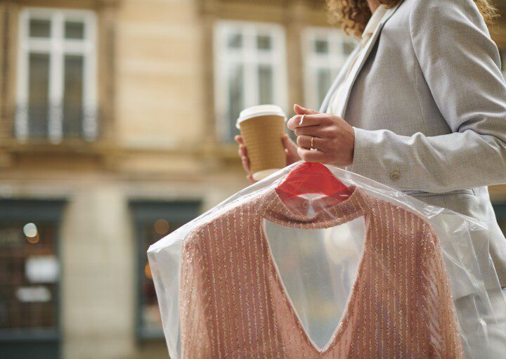 Imagem de uma mulher segurando um café com uma mão e não outra uma peça de roupa recém lavada na lavanderia.