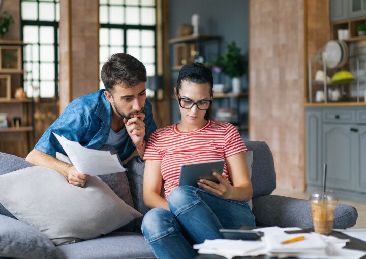 Foto que ilustra matéria sobre porque a parcela do financiamento do imóvel pode aumentar mostra um casal sentado no sofá e vendo papéis