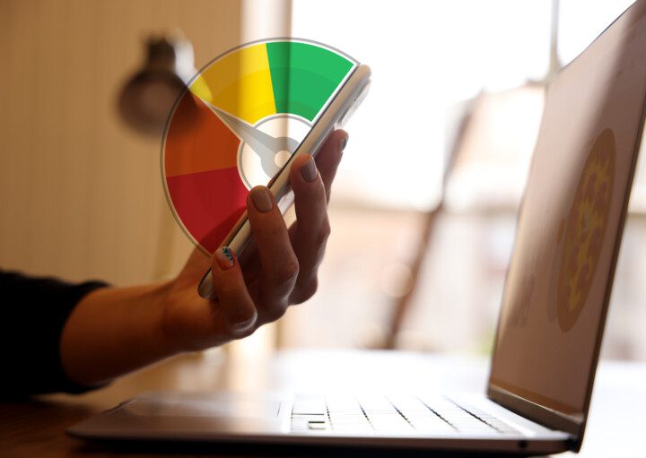 Foto que ilustra matéria sobre Score de Crédito mostra uma pessoa sentada em frente ao computador segurando um celular na mão.