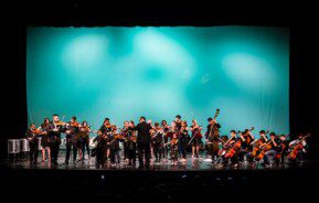 Foto que ilustra matéria sobre o Teatro Municipal de São José dos Campos mostra o interior do espaço com uma orquestra tocando no palco