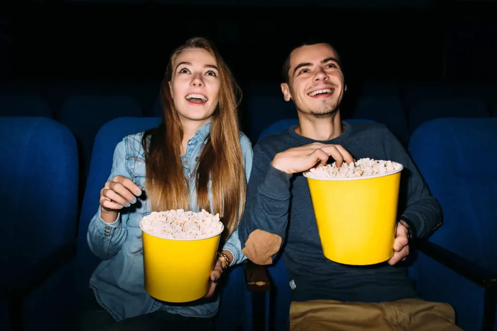 Imagem de duas pessoas em uma sala de cinema comendo pipoca em um balde amarelo para ilustrar matéria sobre que horas abre o shopping de Praia Grande