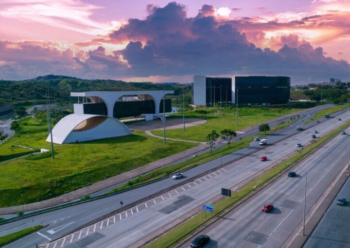 Foto que ilustra matéria sobre a Cidade Administrativa de Minas Gerais mostra o complexo de prédios visto do alto. Ao fundo, um céu rosado no entardecer.