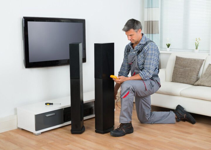 Imagem de um homem em uma sala de TV instalando um home theater.