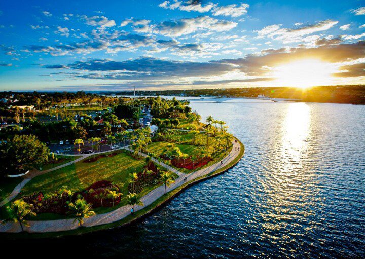 Foto que ilustra matéria sobre o Lago Paranoá mostra o espelho d'água ao Centro, com um pôr do sol à direita e uma das margens do lago, com uma área verde, à esquerda.