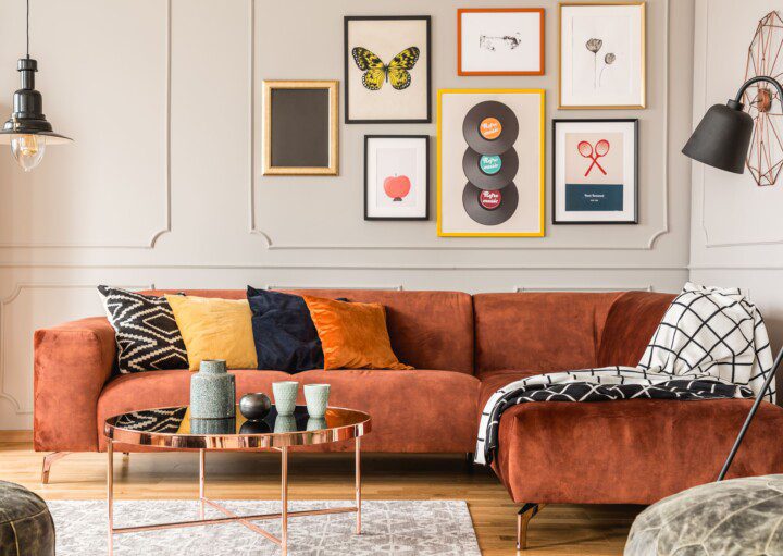 Sofá terracota, com almofadas coloridas, mix de quadro na parede, luminária e detalhe de boiserie.