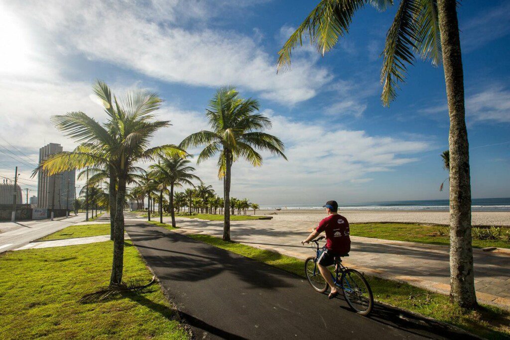 Foto que ilustra matéria sobre a Região Metropolitana da Baixada Santista mostra um ciclista pedalando na ciclovia da orla de uma das praias da cidade