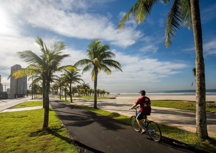 Foto que ilustra matéria sobre o que fazer em Praia Grande mostra um ciclista pedalando na ciclovia da orla de uma das praias da cidade