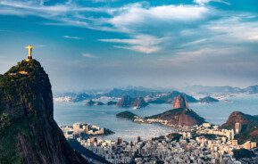 Imagem da vista aérea do Morro do Corcovado que mostra parte dos prédios, morros e praias do Rio de Janeiro