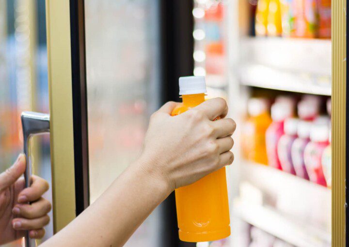 Um pessoa pega um suco de laranja em uma geladeira de mercadinho em condomínio.