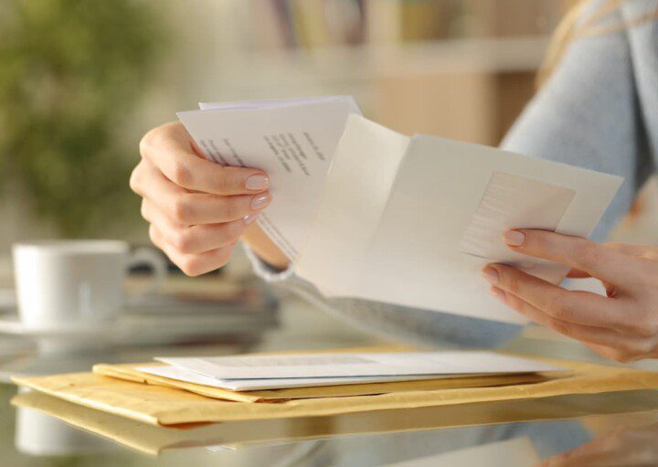 Mãos com características femininas abrem um envelope de carta.