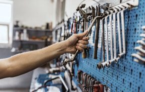 Imagem do braço de um homem pegando uma ferramenta em um painel azul com diversos tipos de chave penduradas