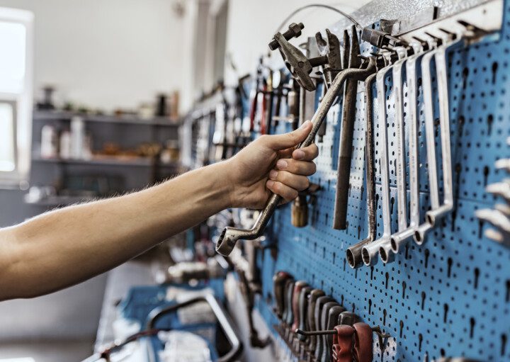 Imagem do braço de um homem pegando uma ferramenta em um painel azul com diversos tipos de chave penduradas
