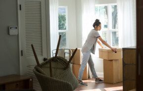 Foto que ilustra matéria sobre sair de casa mostra uma mulher em meio a caixas de mudança no cômodo de um imóvel