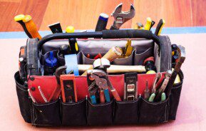 Foto mostra uma bolsa com alça e vários compartimentos repletos de diversos tipos de ferramentas