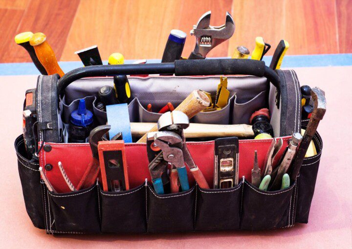 Foto mostra uma bolsa com alça e vários compartimentos repletos de diversos tipos de ferramentas